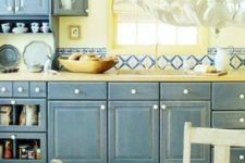 a shabby chic kitchen with shabby blue cabinets, a light yellow backsplash and bright mosaic tiles for a a bold look