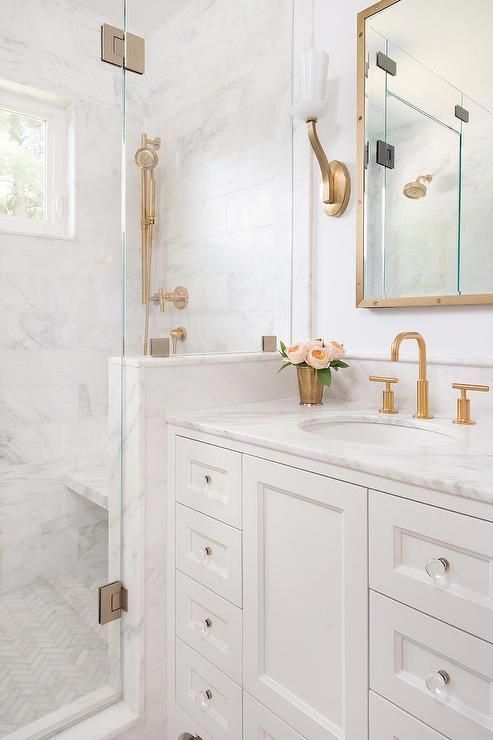 a small white bathroom with a white marble tiles and a countertop, brass and gold fixtures, frames and sconces