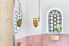 a small yet bold powder room clad with pink tiles, with gold fixtures and a catchy pendant lamp looks wow