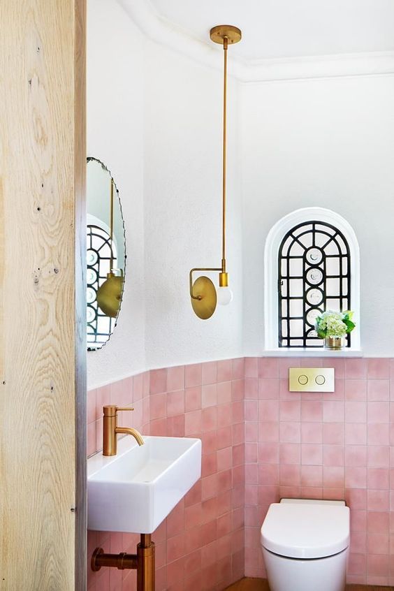 a small yet bold powder room clad with pink tiles, with gold fixtures and a catchy pendant lamp looks wow