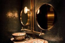 a stylish bathroom with black tiles, gold mirrors, painted sinks and exposed gold pipes is jaw-dropping