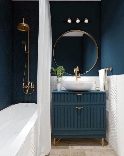 a stylish bathroom with navy walls, navy tiles, a navy vanity, gold frame mirror, gold fixtures and handles