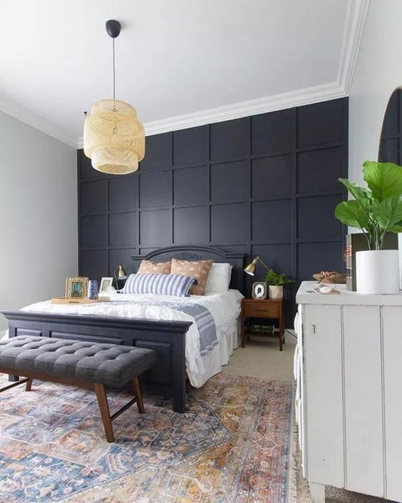 a stylish bedroom in modern and boho styles, with a black paneled wall, a black bed and a grey bench plus a wicker lamp