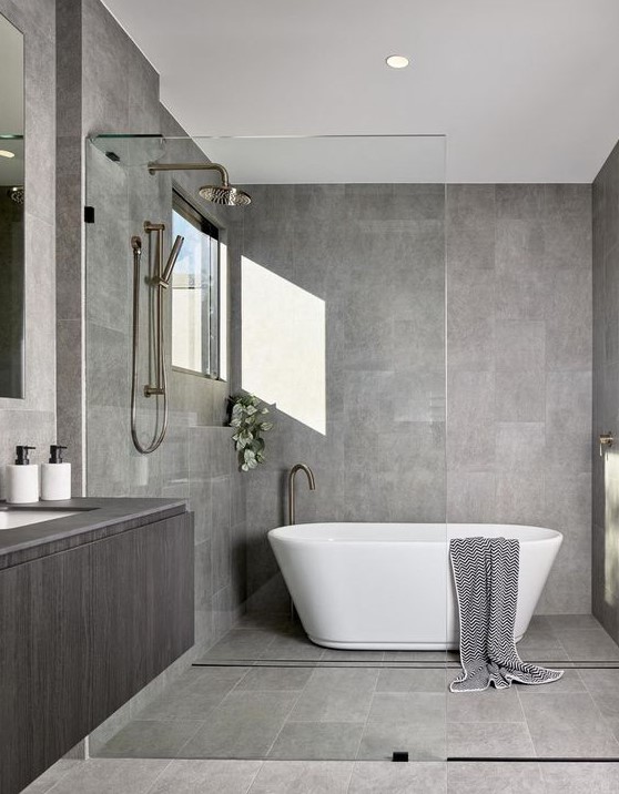 a stylish minimalist bathroom in grey, clad with tiles, with a floating vanity and a free-standing bathtub