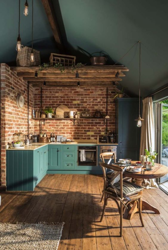 a teal kitchen with a brick wall, a wooden beam installation over the table and a cozy wooden dining set