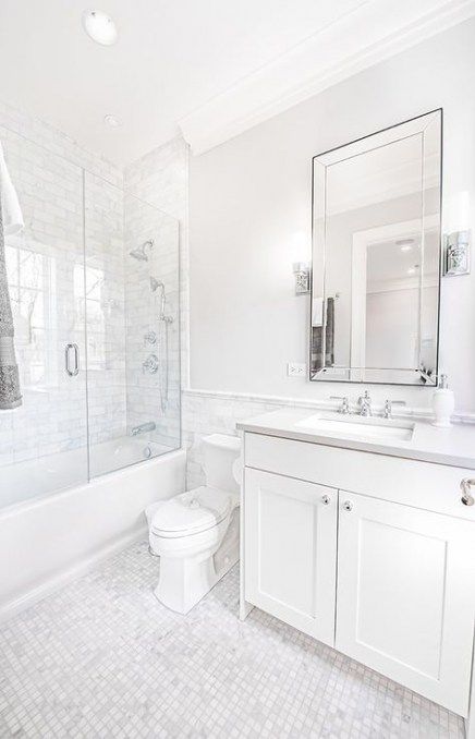 a traditional chic white bathroom with marble tiles, a tub and shower combo, with a vanity and a large mirror