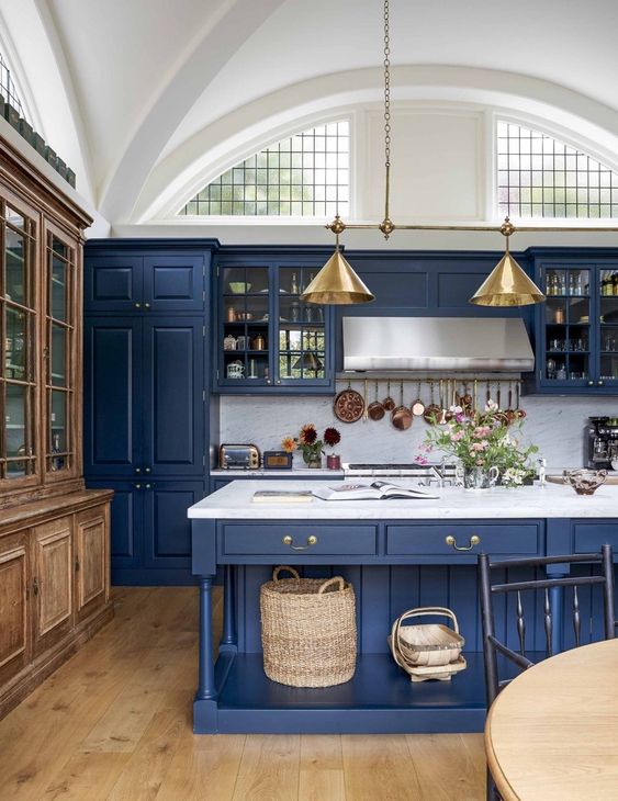 a vintage blue kitchen with white marble countertops and a backsplash, with light borwn floors and a buffet plus touches of gold