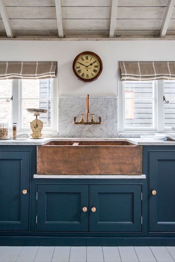 a vintage navy kitchen with a built-in copper hammered sink and a matching faucet to make up a bold look