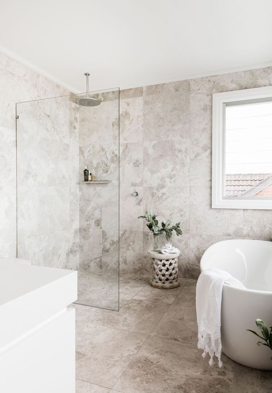 a welcoming neutral bathroom with catchy stone tiles, white appliances and a vanity and some greenery in vases