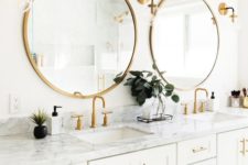 a white bathroom with a large double vanity, a marble countertop, godl framed mirrors, handles and sconces looks nice