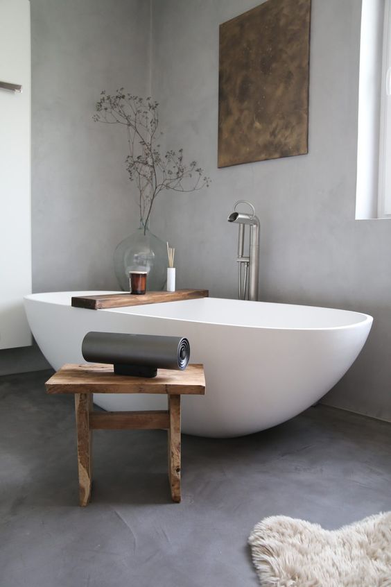 an airy and chic bathroom in grey, with an oval tub, a wooden stool and some minimal decor is super chic