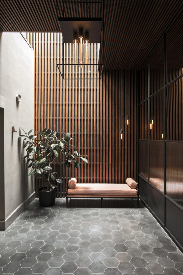 The entryway features grey hex tiles, a pink couch, a potted plant, a skylight and an industrial lamp The entryway features grey hex tiles, a pink couch, a potted plant, a skylight and an industrial lamp
