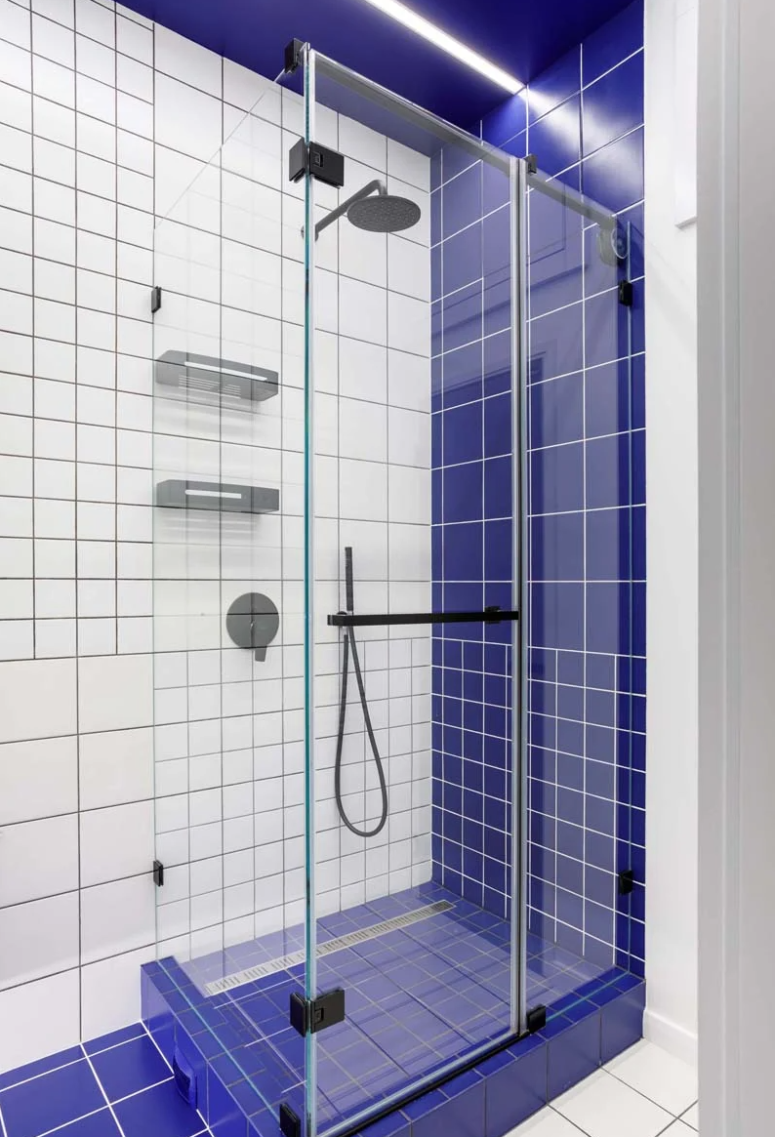 The bathroom is done with white tiles, black grout for achieving a graphic look and bold blue tiles for an accent