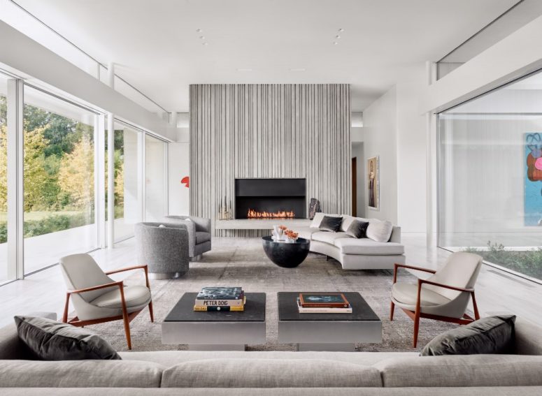 The living room is done in neutrals - white, grey, taupe, with a built-in fireplace, comfy modern furniture and a glazed wall