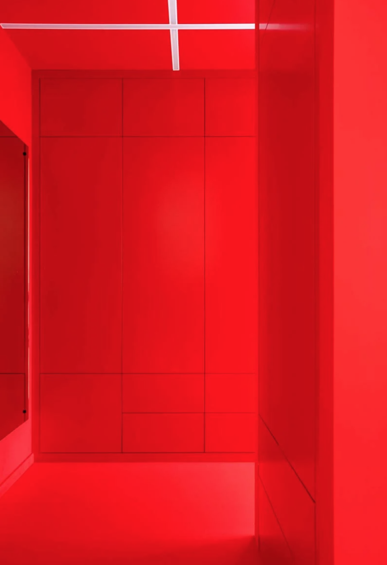 The entryway is bright red, with sleek storage units and a large mirror and built-in lights