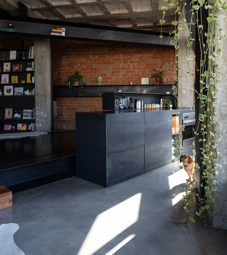 a kitchen with dark furniture and brick walls The furniture is made of darkened metal, there are brick walls and some wooden touches to soften the look