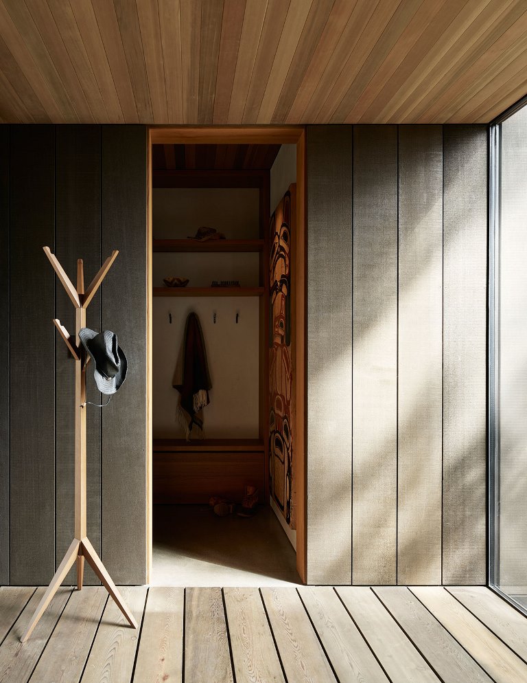 The entryway is clad with sleek and neutral wood and there's a storage space hidden