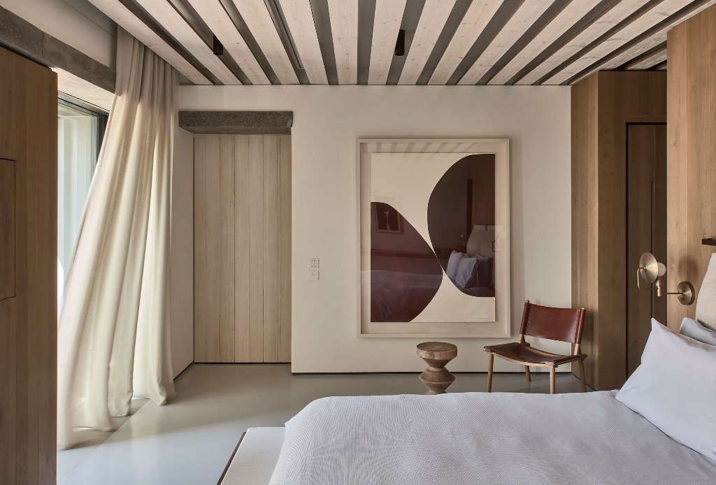 The master bedroom shows off wooden panels, a comfy bed, sconces and a statement artwork