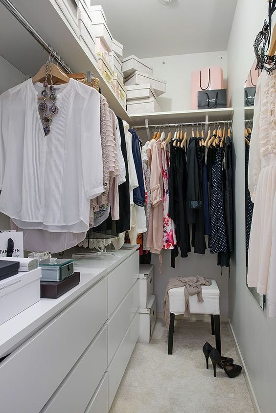 a small contemporary closet in white, with a large open shelf with boxes, dressers, holders with hangers and a stool
