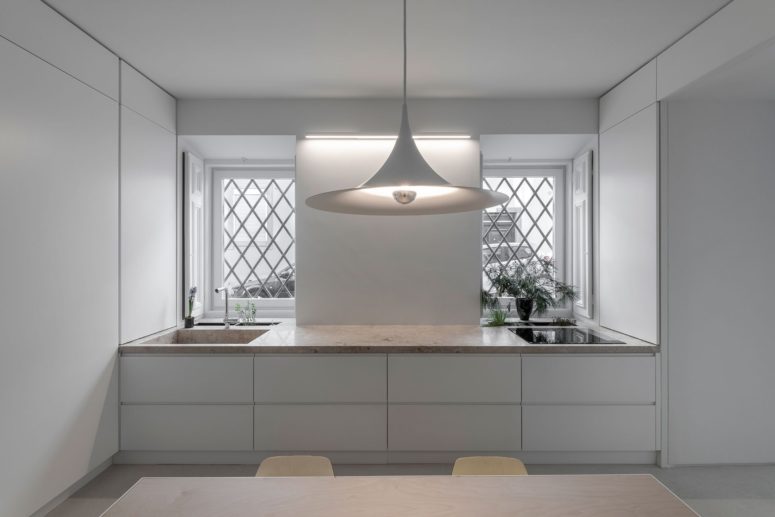 The kitchen is pure white, with sleekcabinets, a stone countertop, a cool pendant lamp