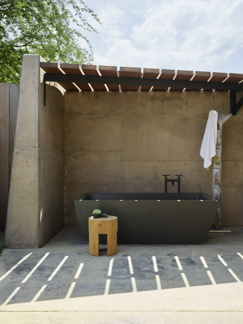 There's an outdoor bathroom designed of concrete and with a large stone tub