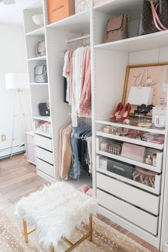 a small glam closet with holders and hangers, built-in drawers, open shelving, artworks, a faux fur stool and a printed rug