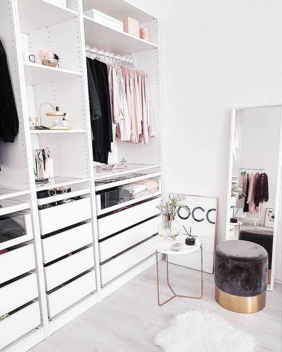 a small glam closet with shelves, a holder for hangers and some drawers, a large window and a cute suede ottoman