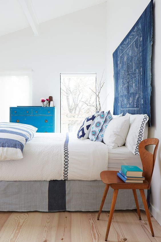 a bold and vivacious bedroom in white, with printed and colorful textiles, a blue tapestry instead of a usual headboard