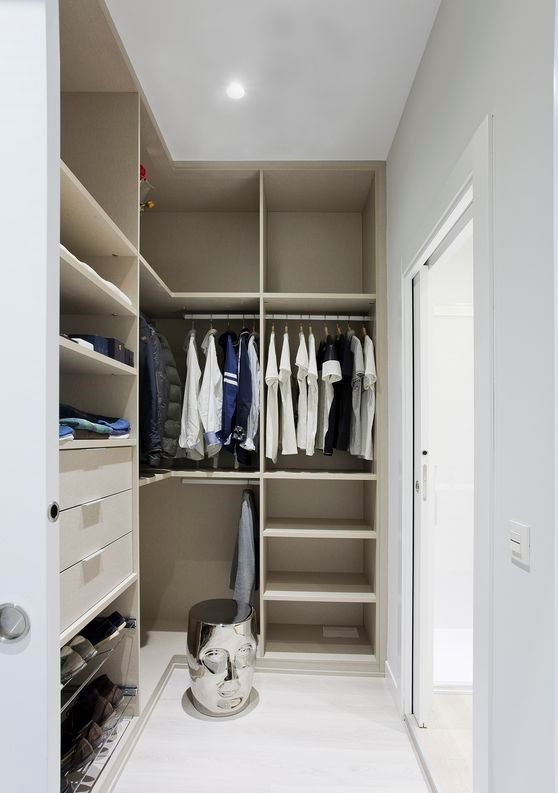 a small minimalist closet with lots of open storage space, dome drawers and holders for hangers, a creative stool and a glass sliding door