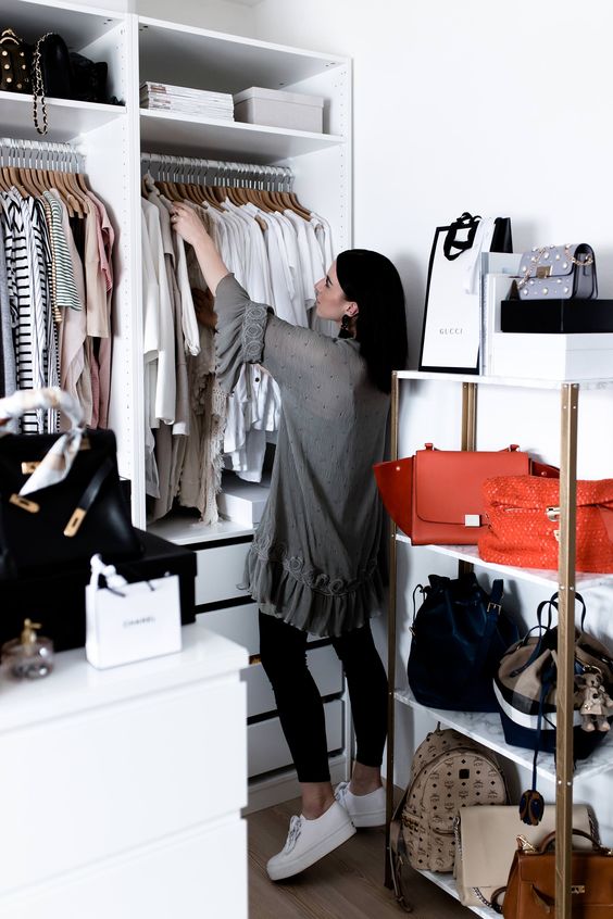 a tiny closet in white, with some open shelves,drawers, holders for hangers, a dresser and an open storage unit for bags