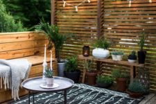a Nordic patio all clad with wood, with a printed rug, some potted greenery and candle lanterns and lights