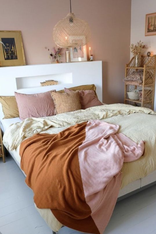 a boho bedroom wiht a mauve accent wall, a bed with a storage headboard, pink and yellow bedding and candles