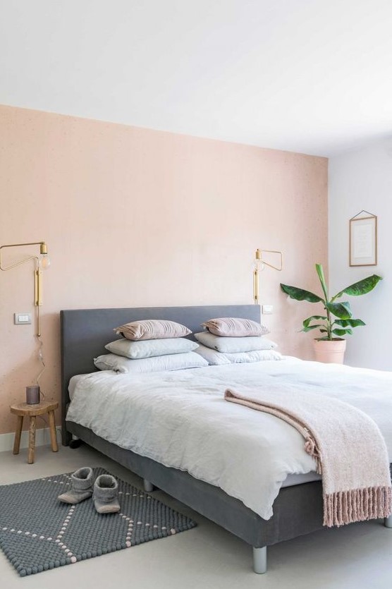 a boho chic bedroom with a light pink accent wall, an upholstered bed, pastel bedding and a printed rug