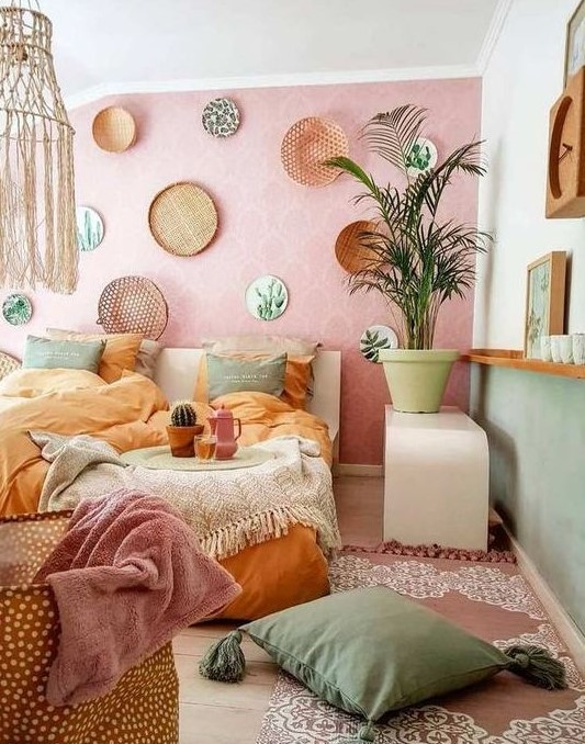a boho pastel bedroom with a pink accent wall and green walls, a bed with muted color bedding, a macrame lamp and pastel pillows