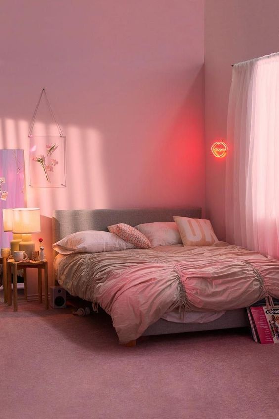 a bold modern pink bedroom with a grey upholstered bed and pink bedding, a nightstand with a table lamp and a neon light