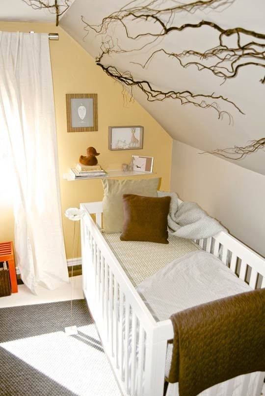 a bright attic nursery with a yellow accent wall, cozy textiles and a rug plus a small gallery wall and branches for a natural touch