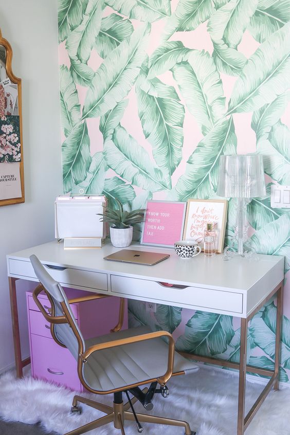 a bright tropical home office nook with a tropical leaf wall, a pink storage unit and art and touches of gold and brass