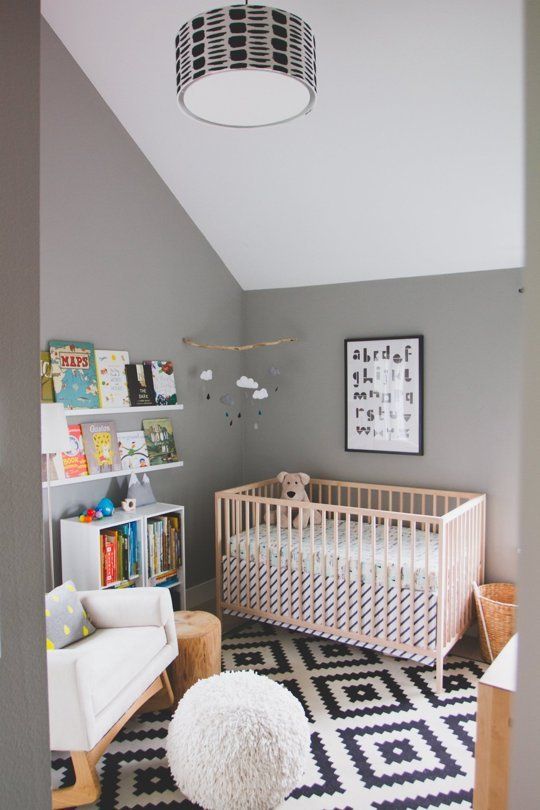 a casual nursery with grey walls and a white ceiling, a printed rug, simple furniture and a bookshelf for reading to your kid