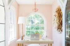 a chic and cozy home office nook with light pink walls, a chic chandelier, a simple desk and an upholstered and acrylic bench
