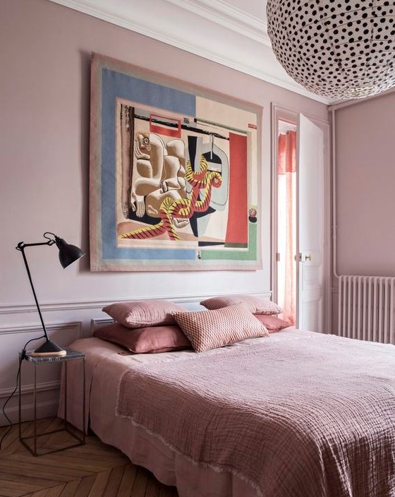 a chic bedroom with light pink walls, pink bedding and a statement artwork and a polka dot lamp