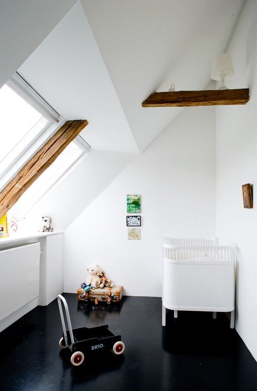 a contrasting attic nursery with a black floor, wooden beams, a white crib, some toys and a bright galley wall