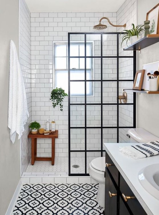 a contrasting black and white bathroom with white subway tiles and printed tiles, a black vanity, a framed screen and brass touches