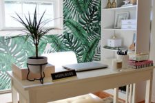 a cool and inviting tropical home office with a tropical leaf wall, woven shades, a tropical plants and touches of pink
