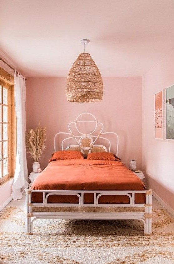 a cool boho pink bedroom with a rattan and cane bed, a large woven pendant lamp, a gallery wlal and a printed rug