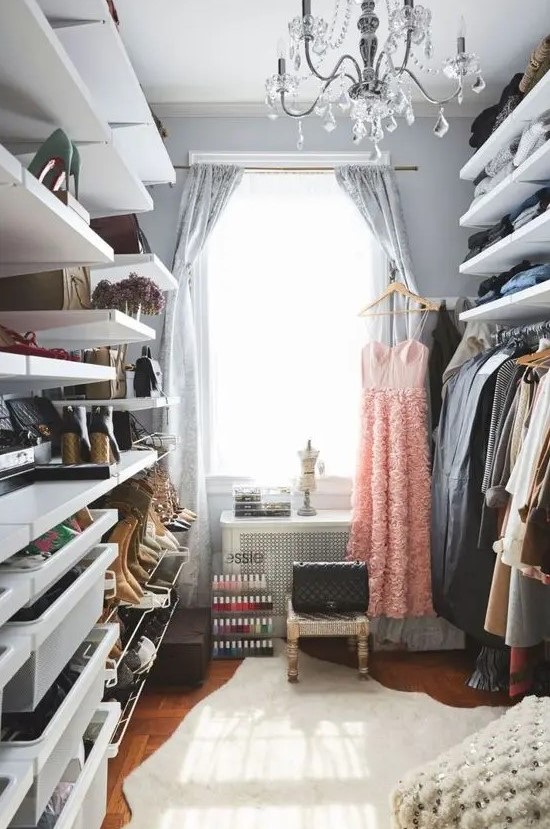 a cool grey closet with open shelves and racks, a bit of drawers, woven stools and a small vanity plus a crystal chandelier