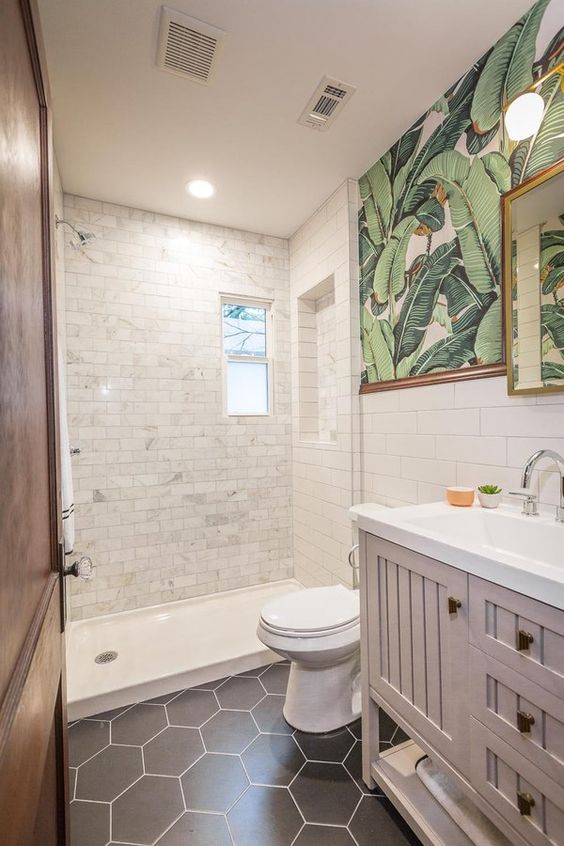 a cool small bathroom with white marble and black hexagon tiles, a pale pink vanity, tropical print wallpaper and a mirror in a gold frame