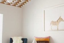 a cozy nursery with a geometric printed ceiling, bright printed textiles, a blue chair and a fun artwork