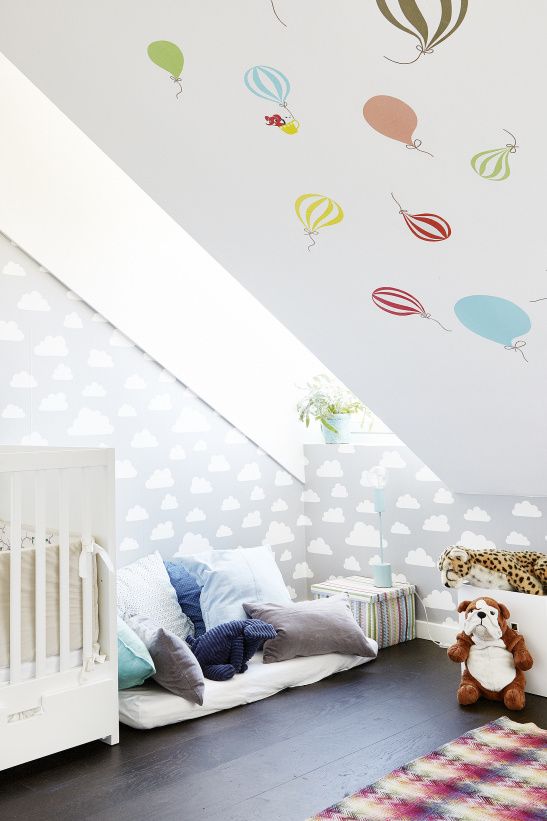 a fun attic nursery with colorful pillows, a hot air balloon wall, a cloud wall and some bold toys