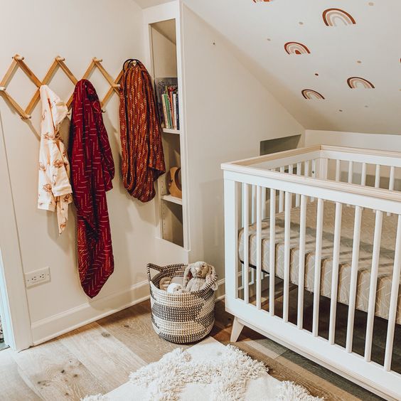 a fun nursery with a rainbow printed wall, a small crib, bright textiles and a storage unit by the bed