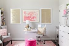 a glam home office with a pink printed rug, gold and pink gallery walls, a hot pink ottoman and a fluffy pillow